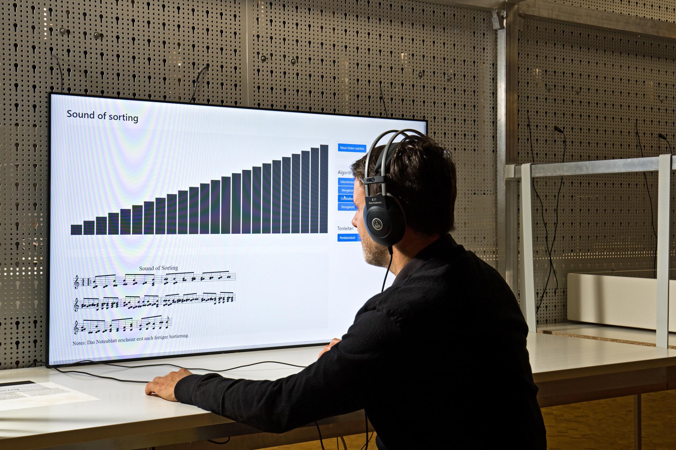 Das Bild zeigt einen sitzenden Mann mit Kopfhörern vor einem großen Bildschirm mit einem Soundsimulationsprogramm