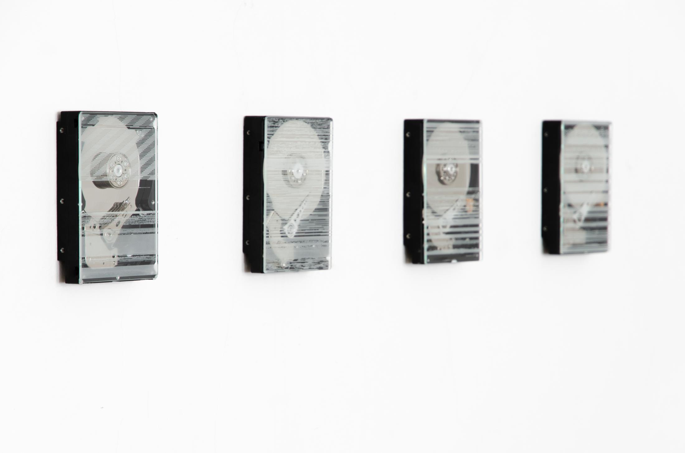 Four hard drives hang in a row on the wall. They are covered with a glass with engravings