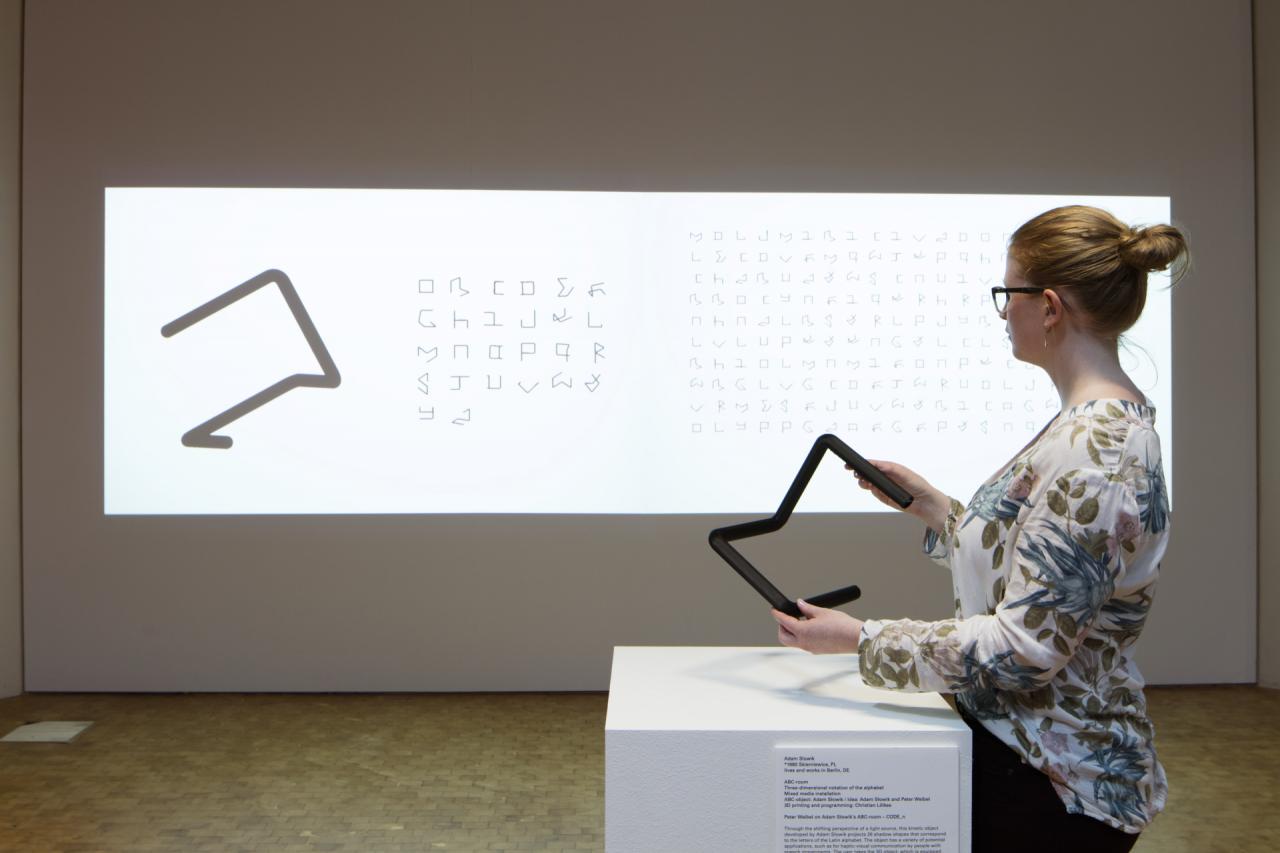 A woman holding a black object in front of a canvas with letters