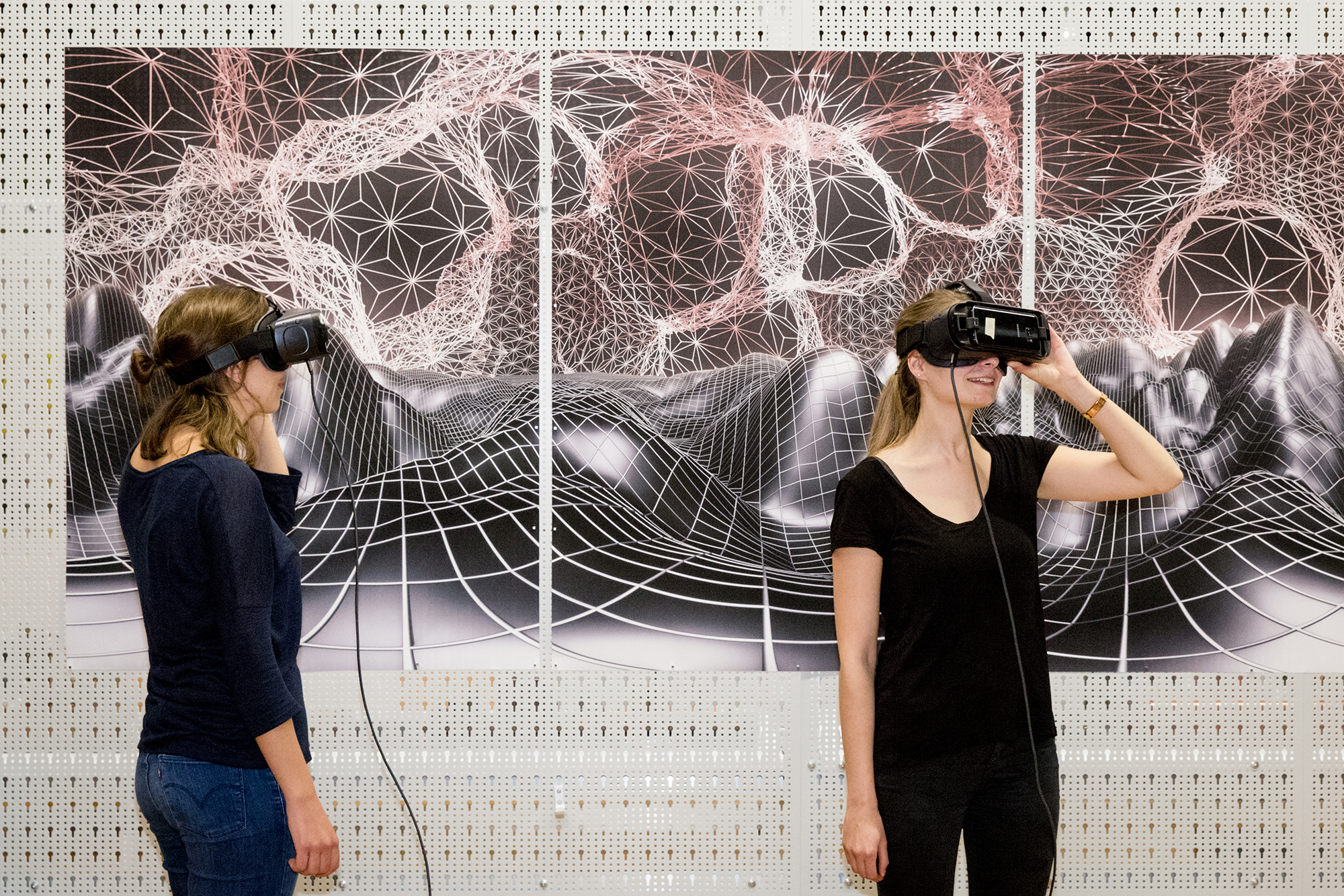 Two women with VR glasses stand in front of a graphic landscape