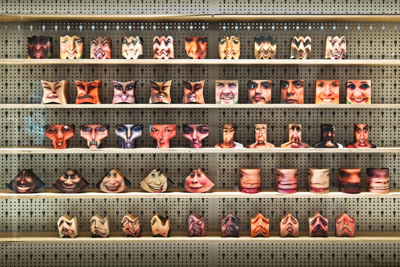 Installation view of various objects with raised faces on a shelf