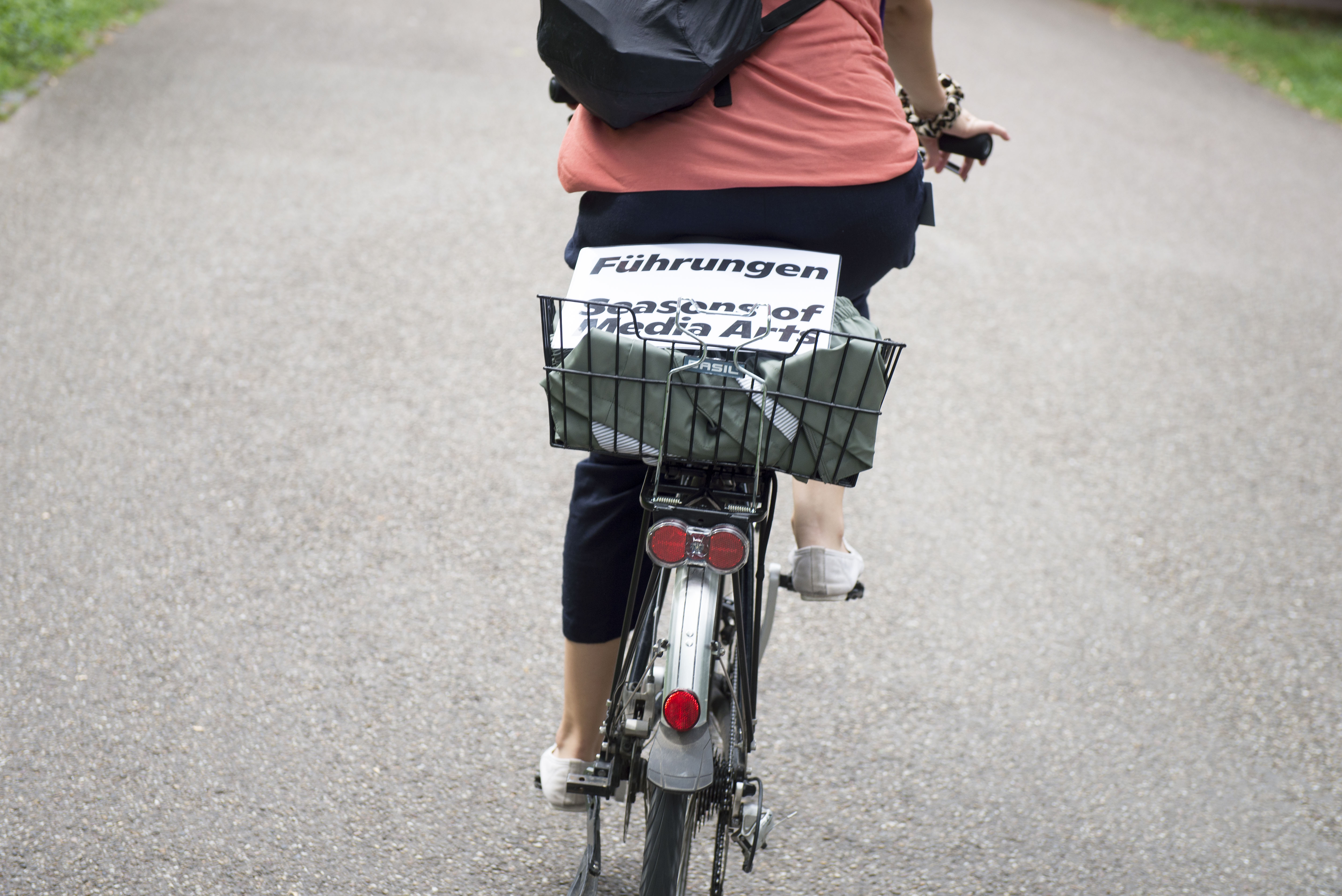 In einem Fahrradkorb liegt ein weißes, laminiertes Schild, darauf steht »Führungen Seasons of Media Arts«