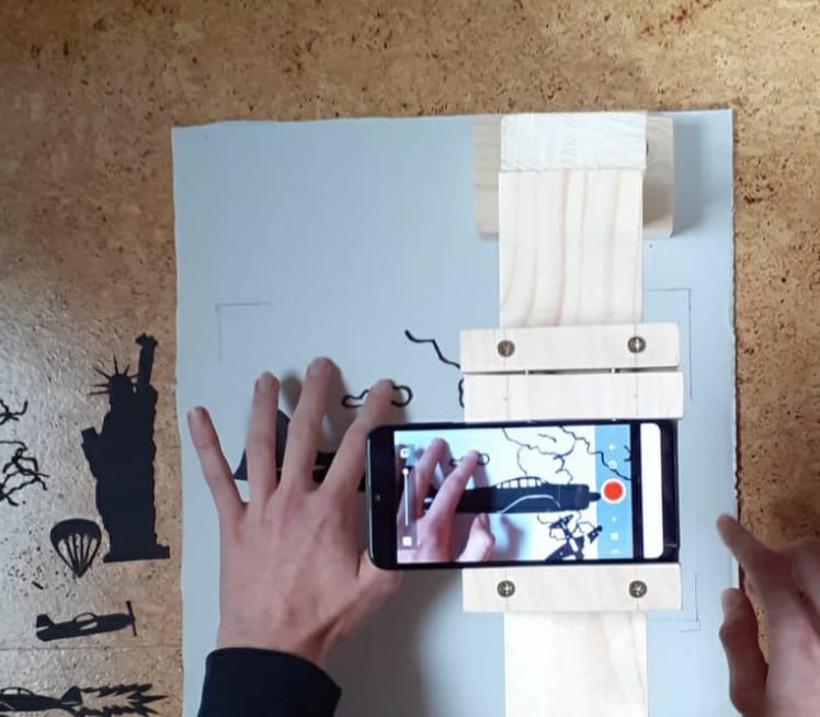 The image shows a hand, various materials and stencils, and a mobile device as a close-up. The image was created as part of the Cultural Academy Baden-Württemberg 2020/21.