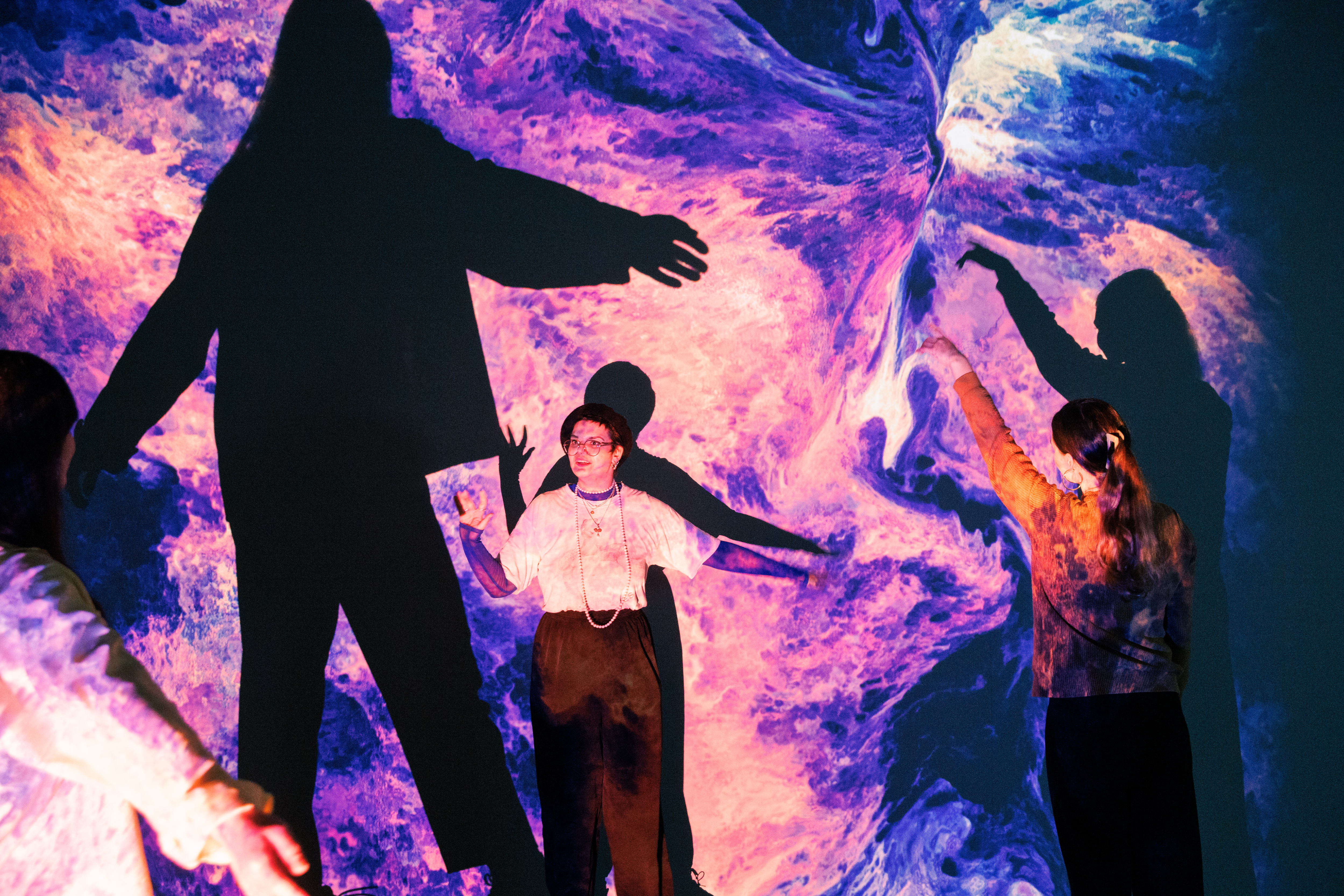 On display is a large canvas, which is covered with an organic, blue and pink pattern. In front of it are three people stretching their arms upwards.