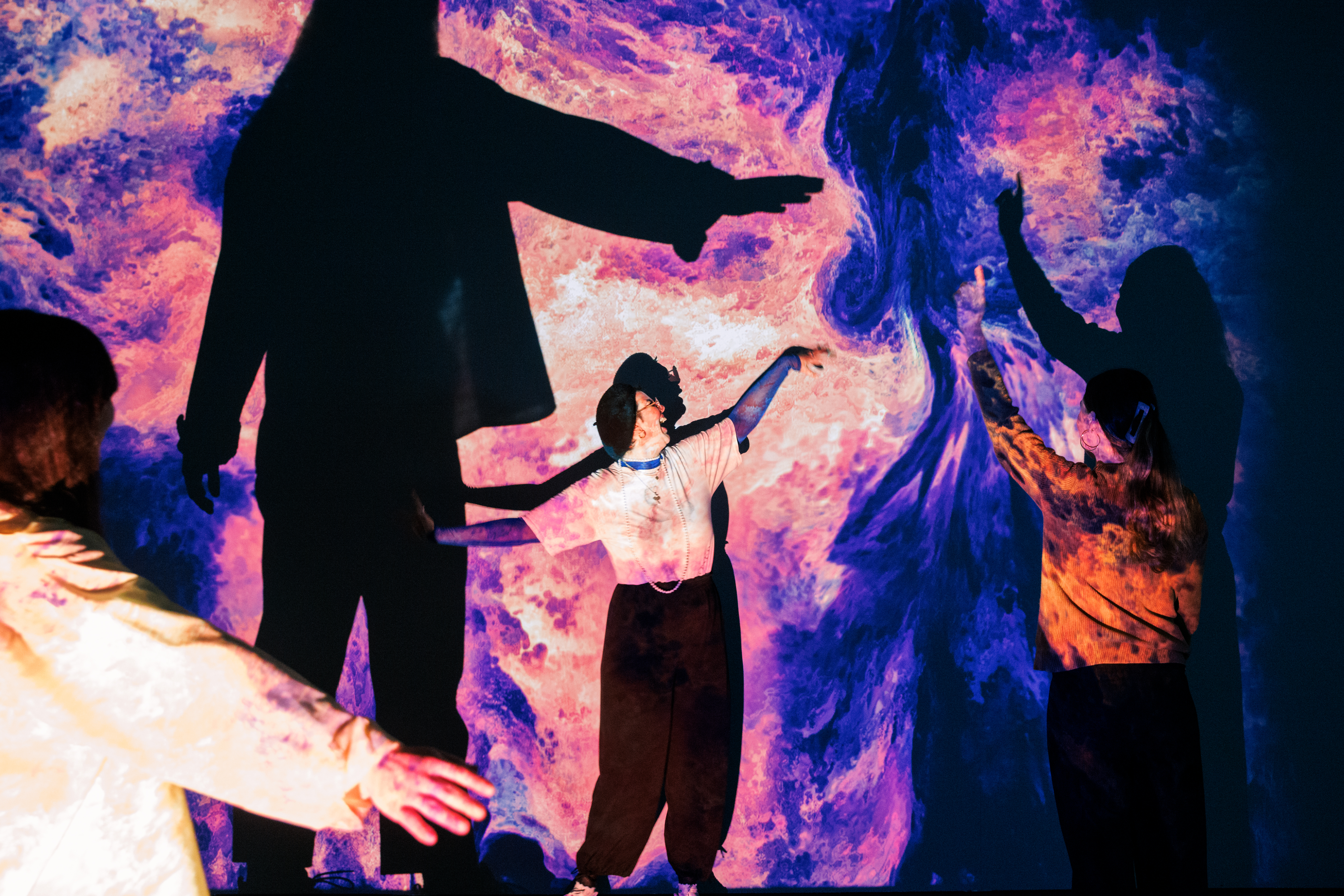 On display is a large canvas, which is covered with an organic, blue and pink pattern. In front of it are three people stretching their arms upwards.