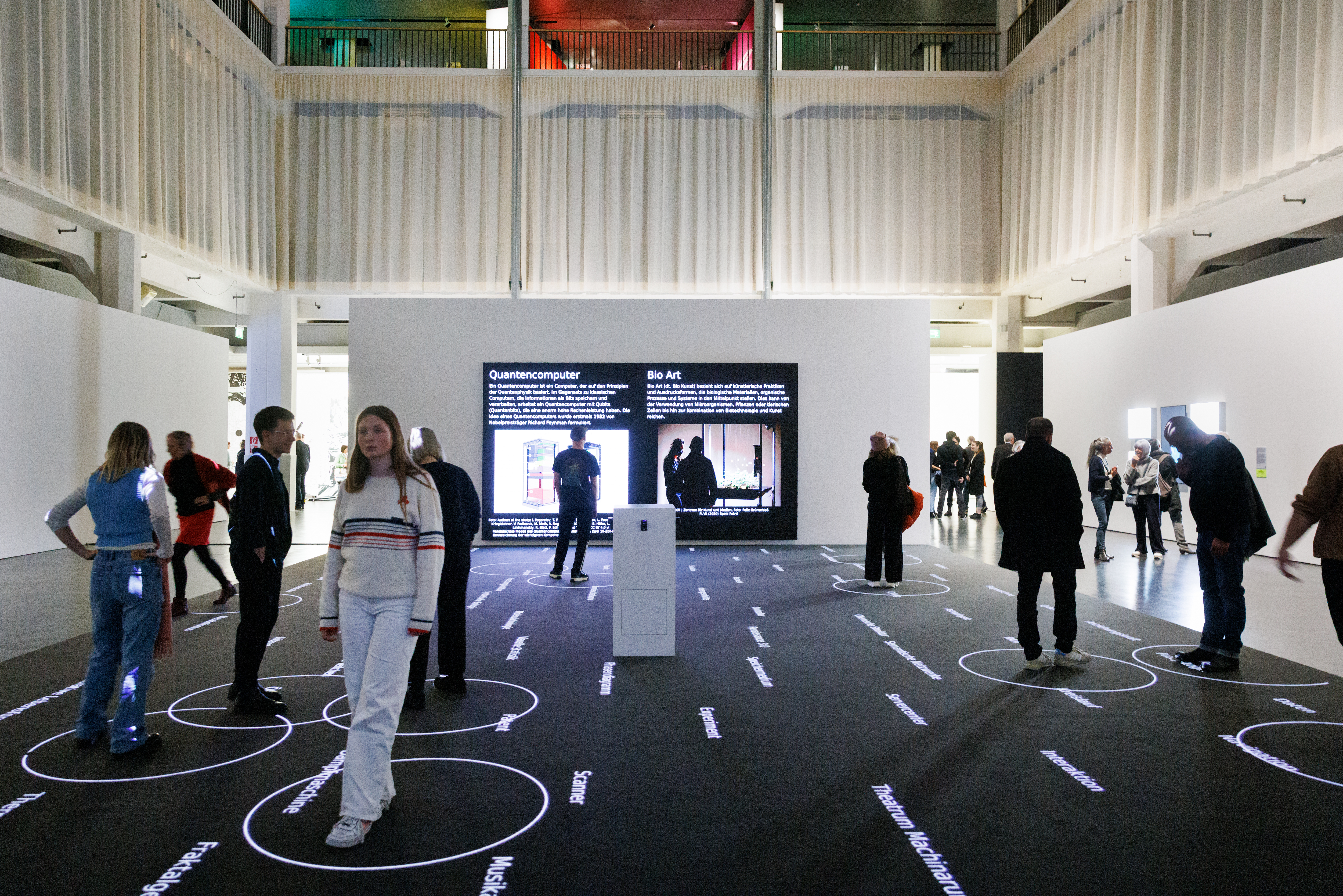 You can see several people on a black surface. On this surface there are words. Around the people are white circles. In the background are two screens.