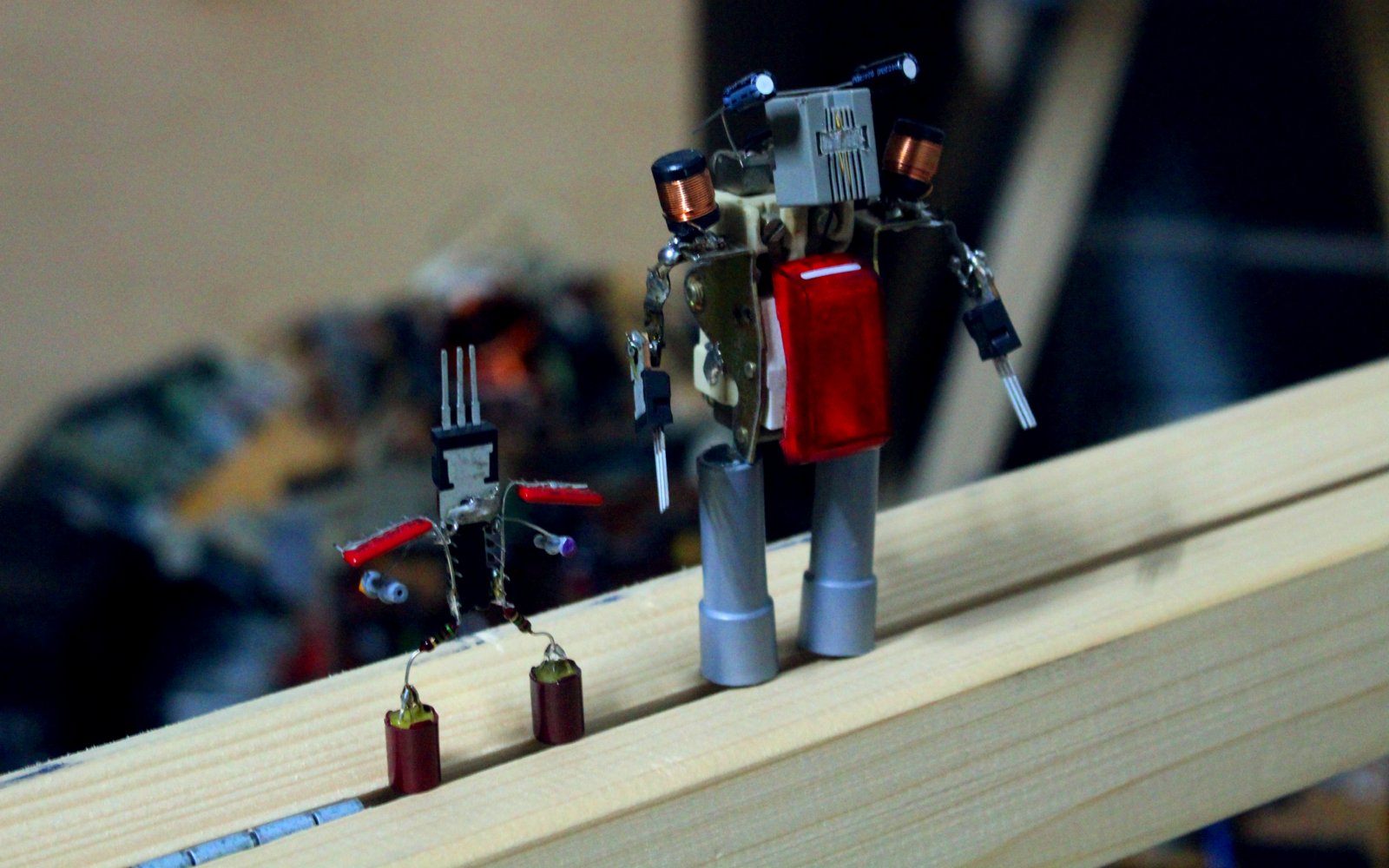 On a timber there are standing two little robots that are soldered together out of electronic scrap.