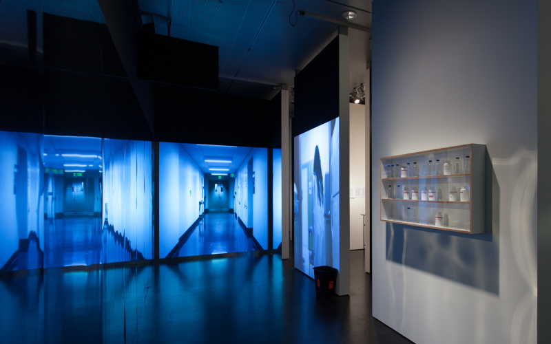 A room with a projected door on the opposite wall. On the right side a shelf with empty bottles.