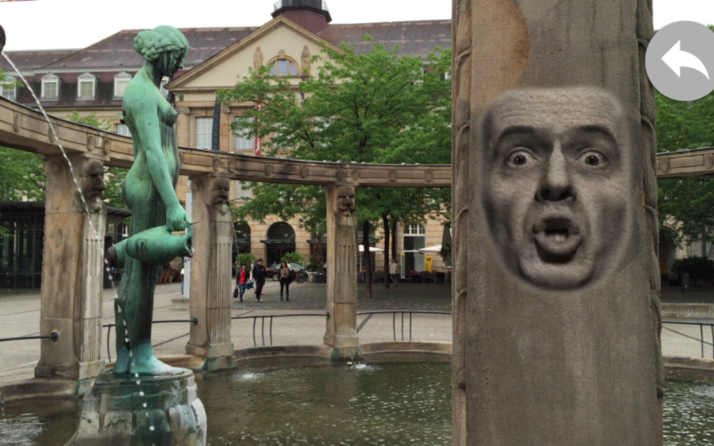 Blick auf den Stephanienbrunnen am Stephansplatz: auf der Säule ist die Projektion eines sprechenden, männlichen Gesichts zu sehen.