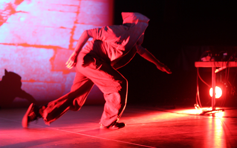 A man on stage with hooded jacket dipped in red light