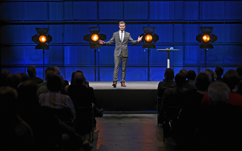 A man in a suit, standing on a stage.