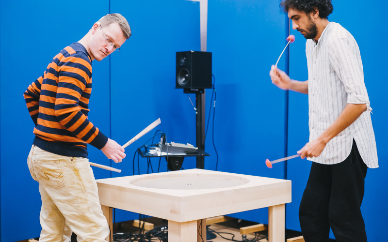 Two men with mallets stand at a table which has a round plate in the middle.