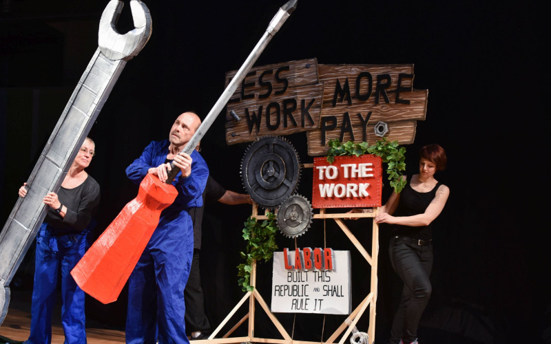 Three people fiddling with oversized tools made of paper mache