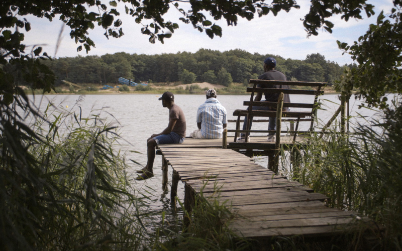 Three men sitting on a pier at a lake