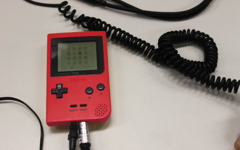 A red gameboy lies on the table and around that some cables.