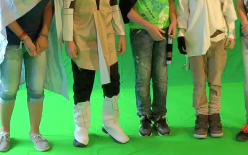 Five kids are standing in front of a greenscreen - only their legs are visible