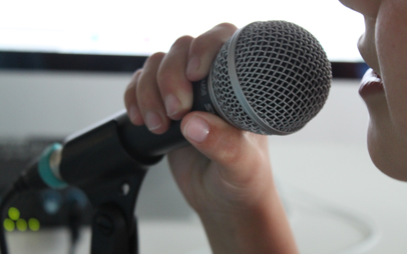 A kid is speaking into a microphone that he is holding infront of his mouth.