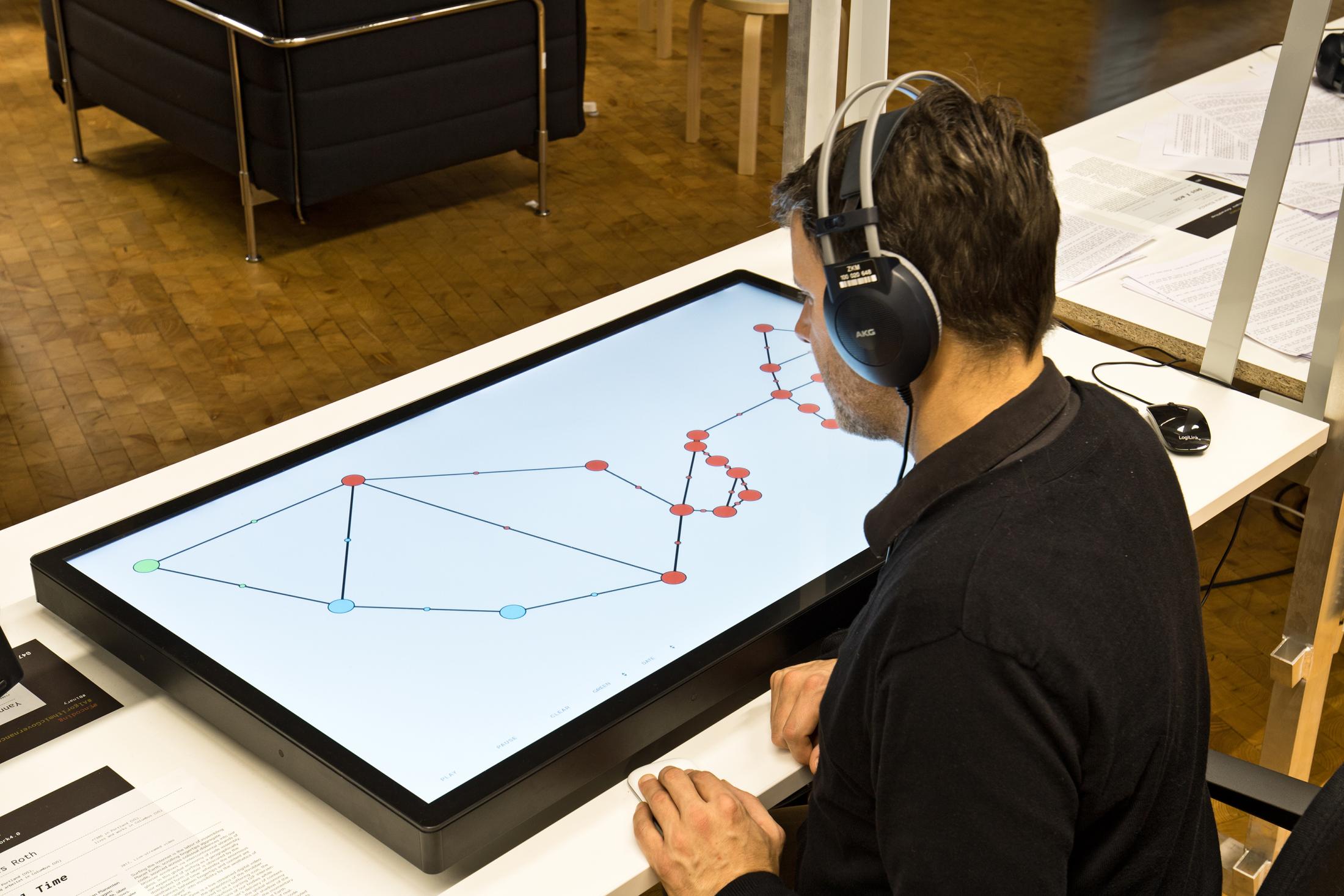 A man has headphones on and sits in front of a large screen lying on the table, which shows a graphic structure