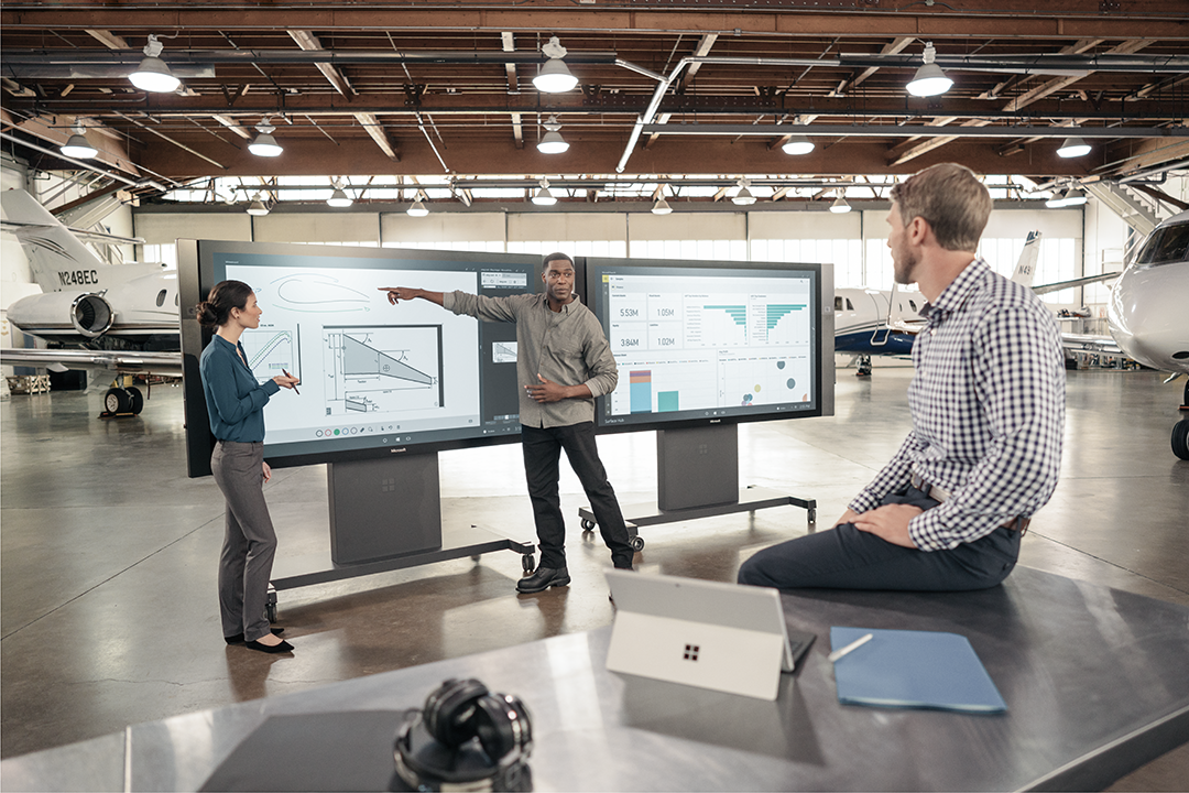 Three people working on digital screens in an aircraft hangar