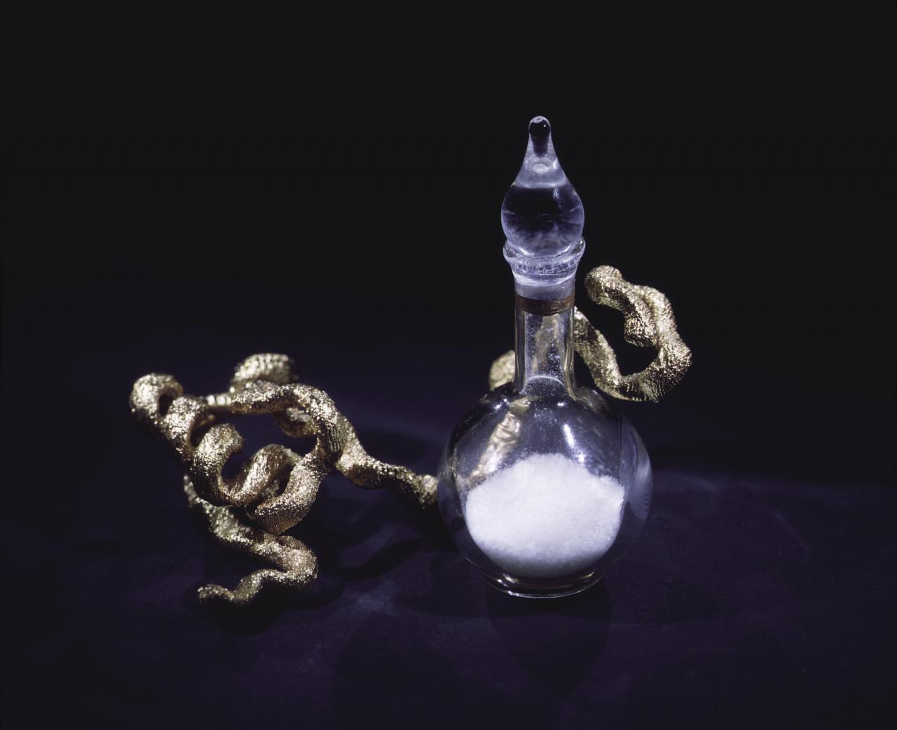 Sculpture of a glass vessel with white content and a golden cast in front of a black background