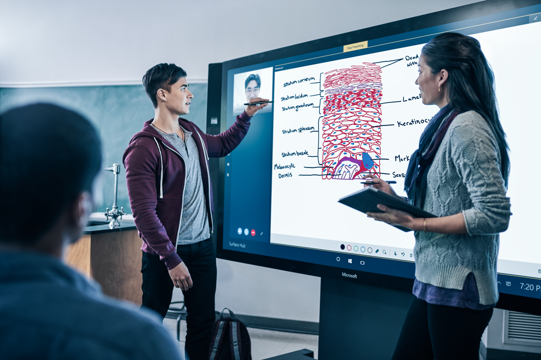 A man and a woman are standing in front of a big screen