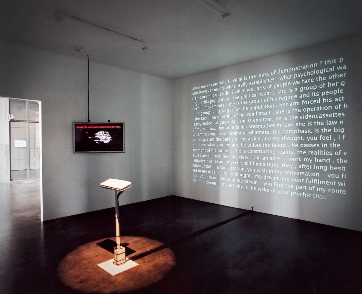 In the middle of a space you can see a keyboard. On one wall hangs a screen, on another wall a text is projected.