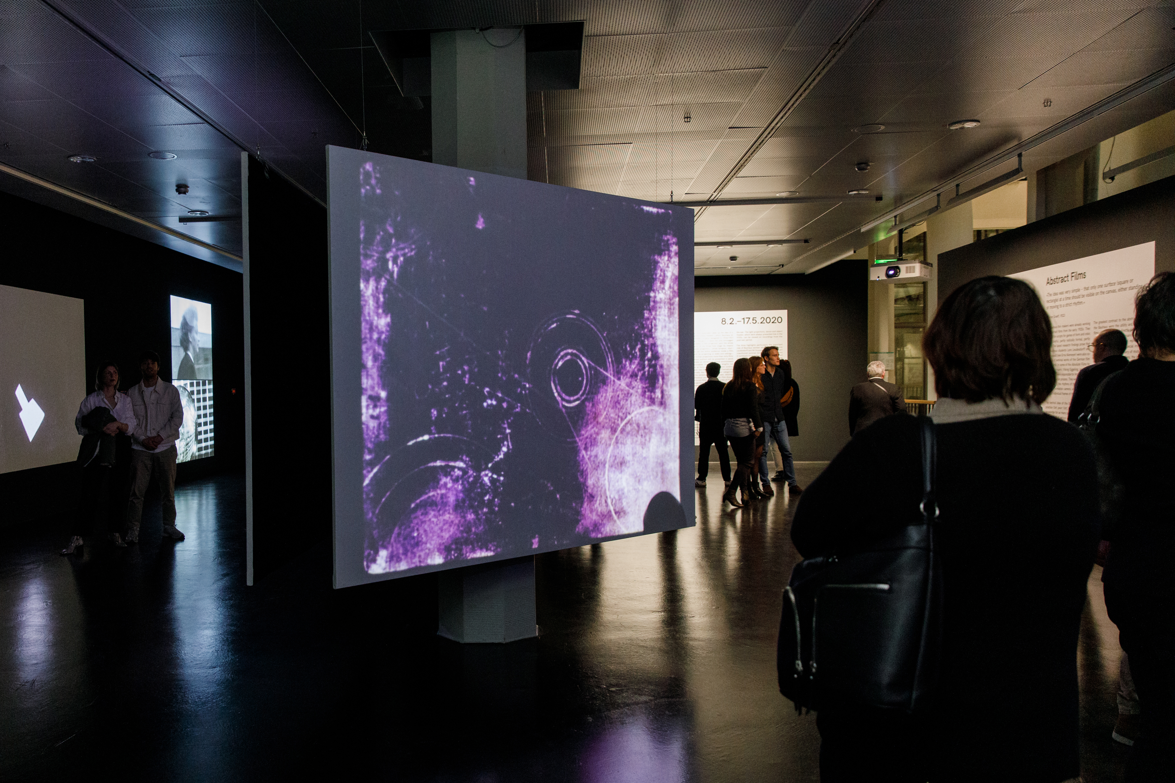 Foto von Menschen vor einer Leinwand mit einem abstrakten Video in Lila – Eine Impression der Ausstellung »bauhaus.film.expanded« am ZKM Karlsruhe.