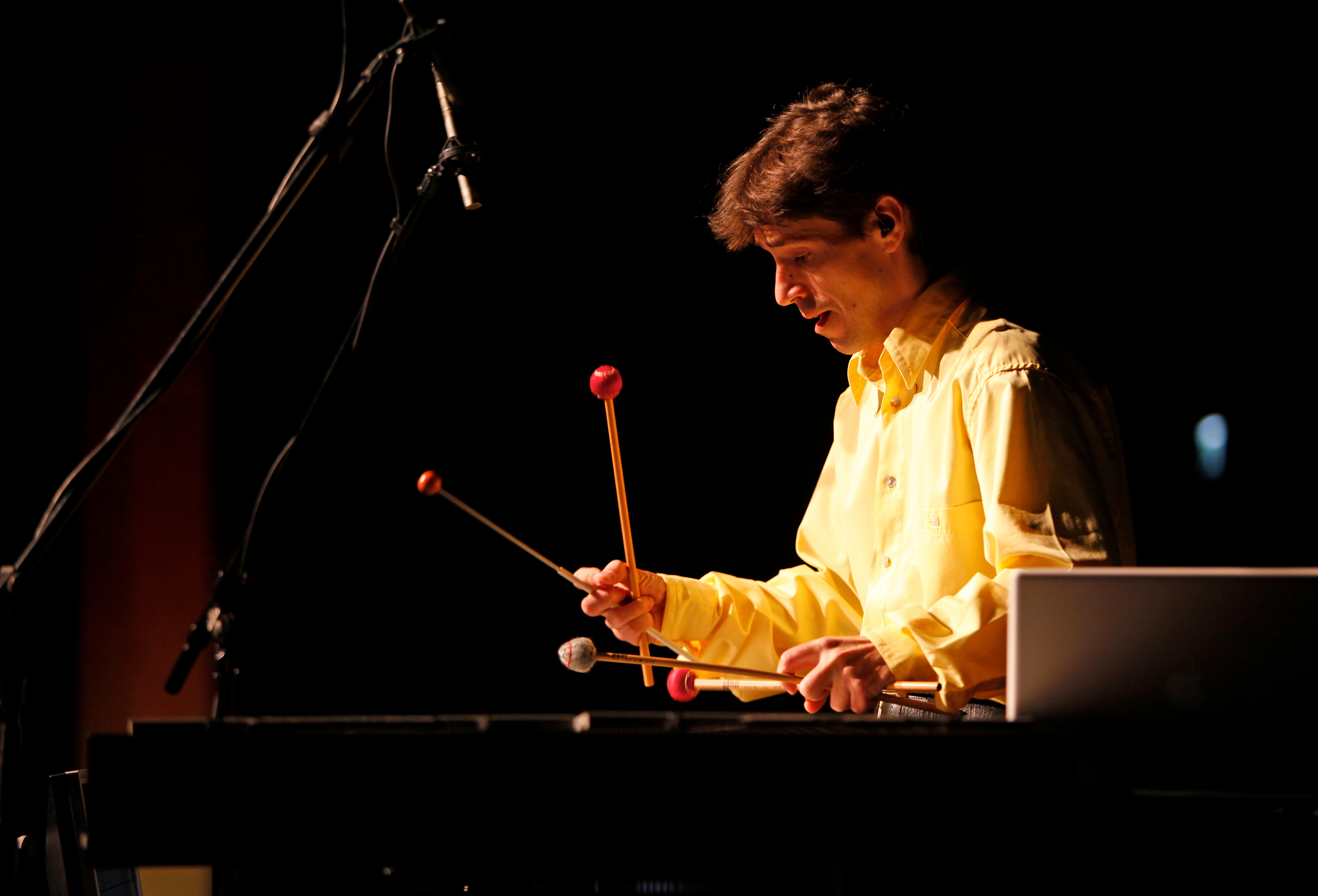 A man is playing on a big xylophone with four beaters holding two in each hand.