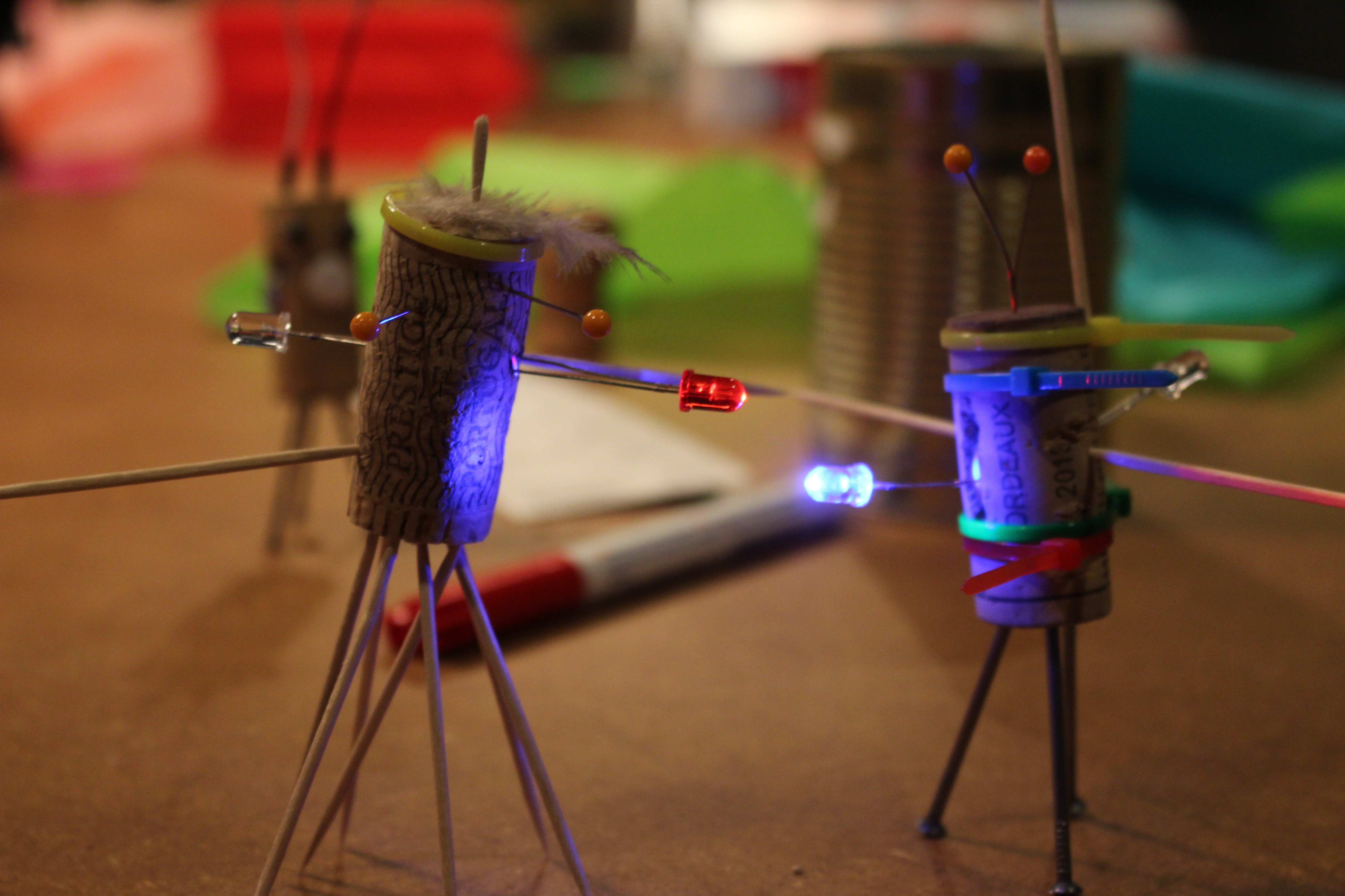 A pair of korks, that are turned into little figurines with LEDs are sitting on a table with crafting materials around them.