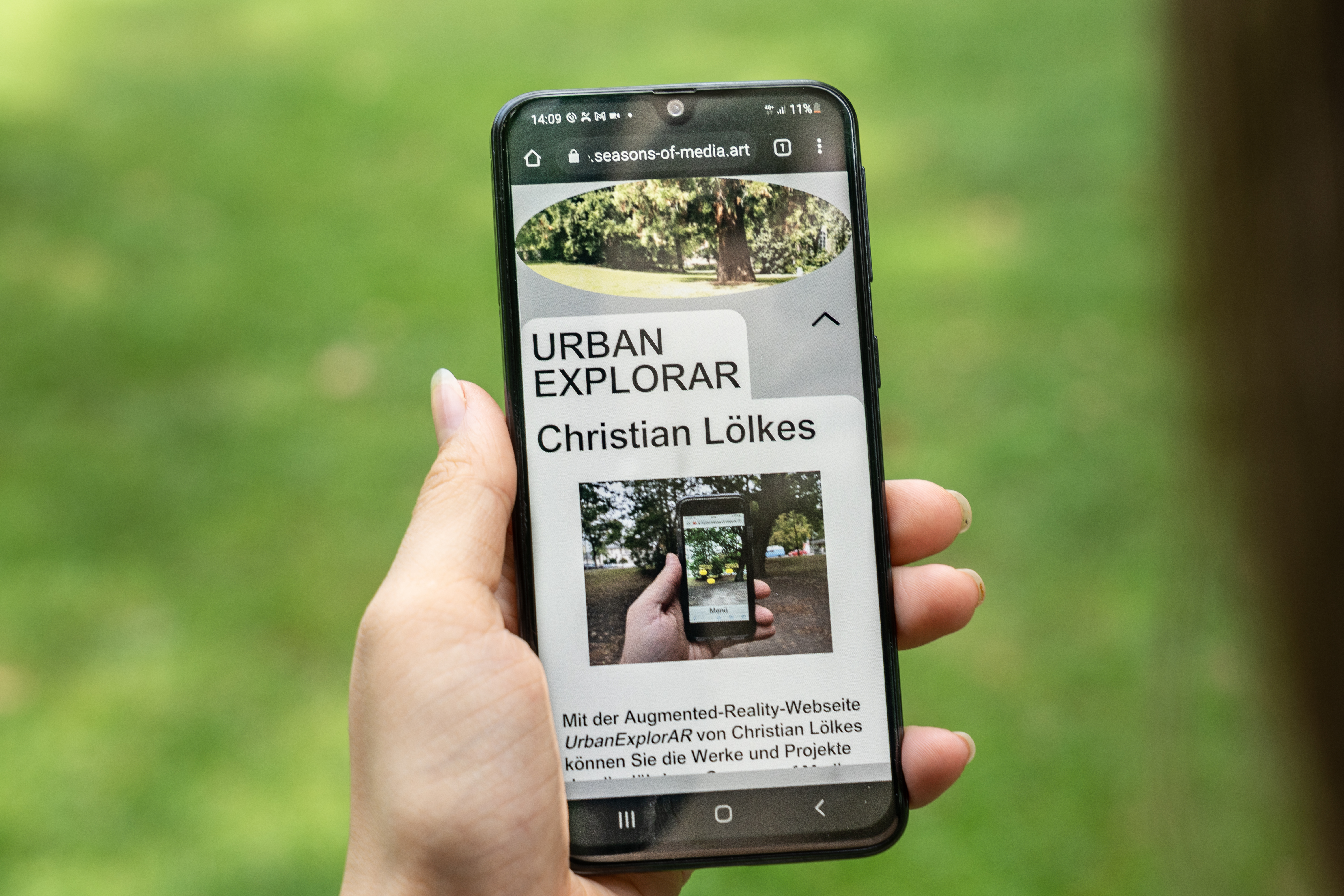 Auf dem Bild ist eine Hand zu sehen, die ein Smartphone hält, auf dem das Werk »UrbanExplorAR« zu sehen ist.