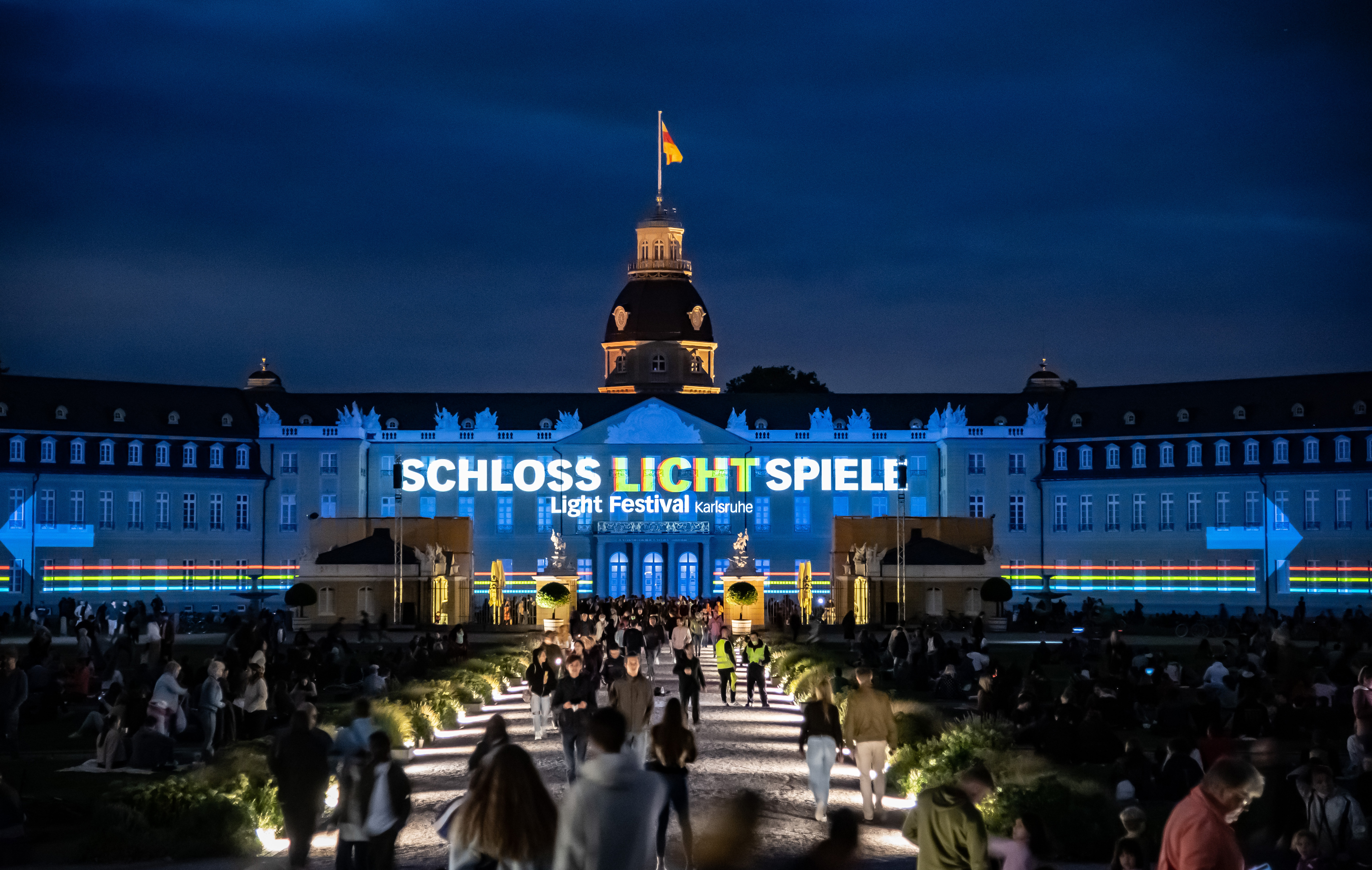 Foto eines bunten Projection Mappings bei Nacht auf dem barocken Karlsruher Schloss. Zu sehen ist der Text »Schlosslichtspiele«