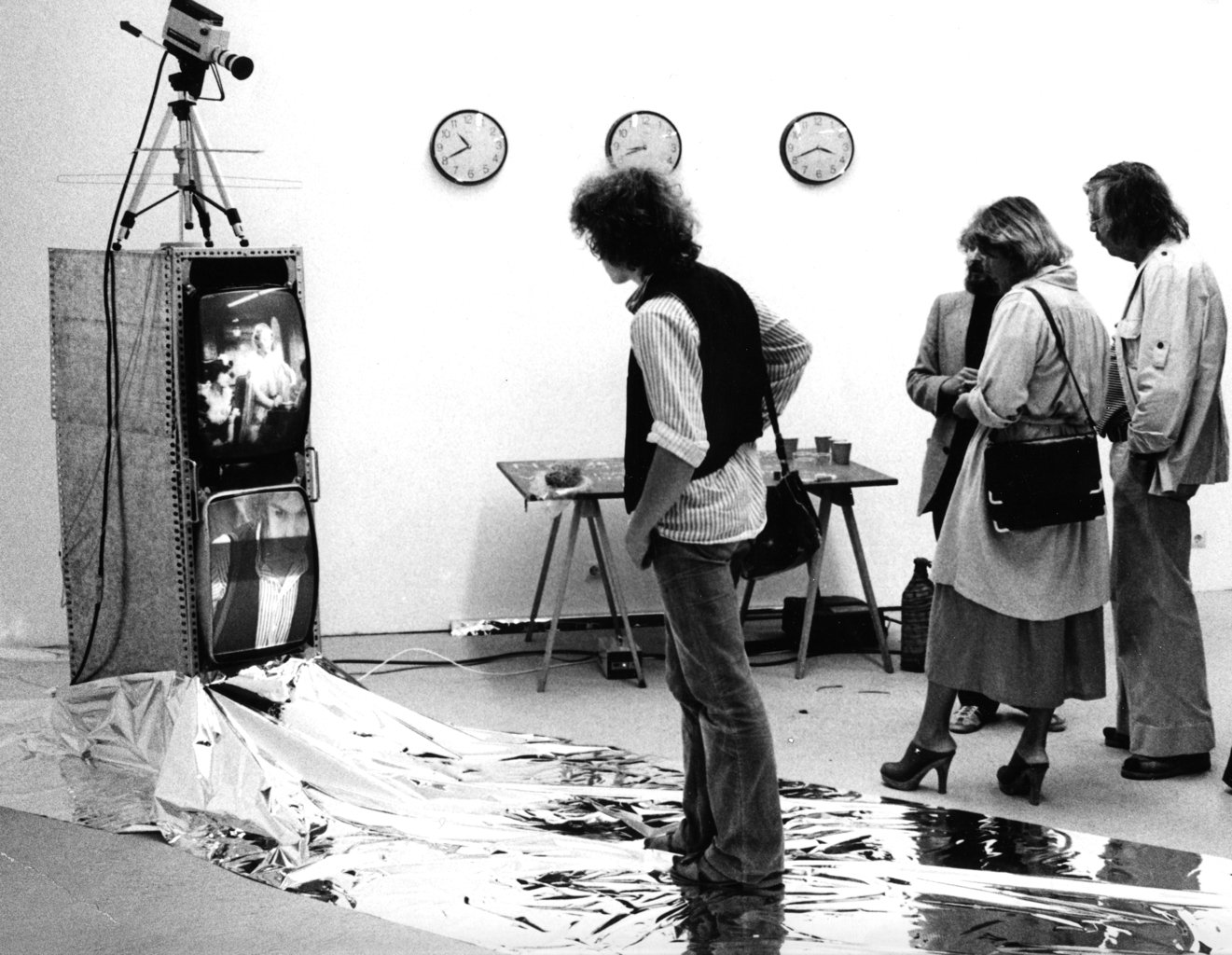 A man is standing on a silver foil and looks at a video installation.