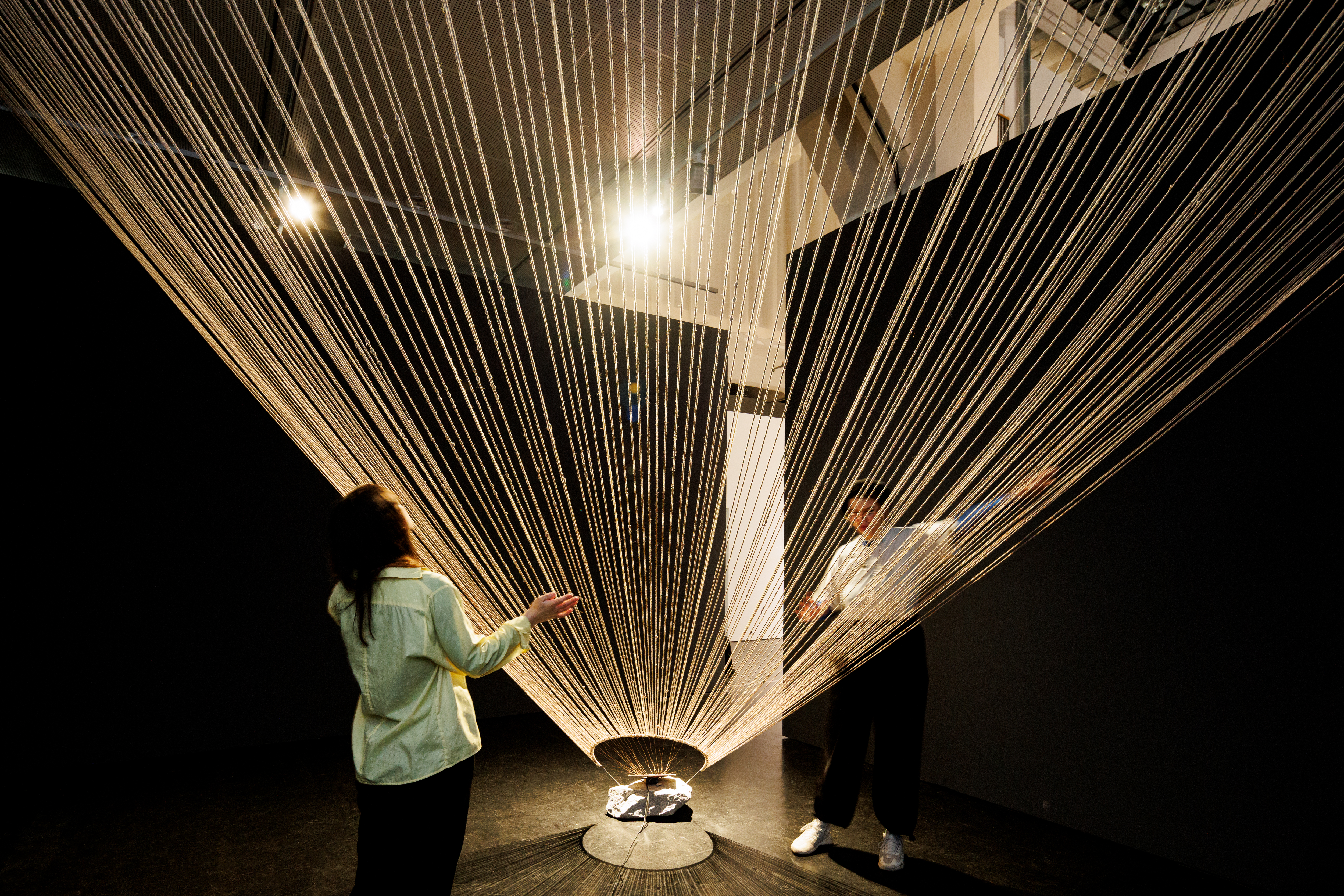 You can see a ceiling-high, wide net made of ropes. Two people are standing next to it, one on the left and one on the right.