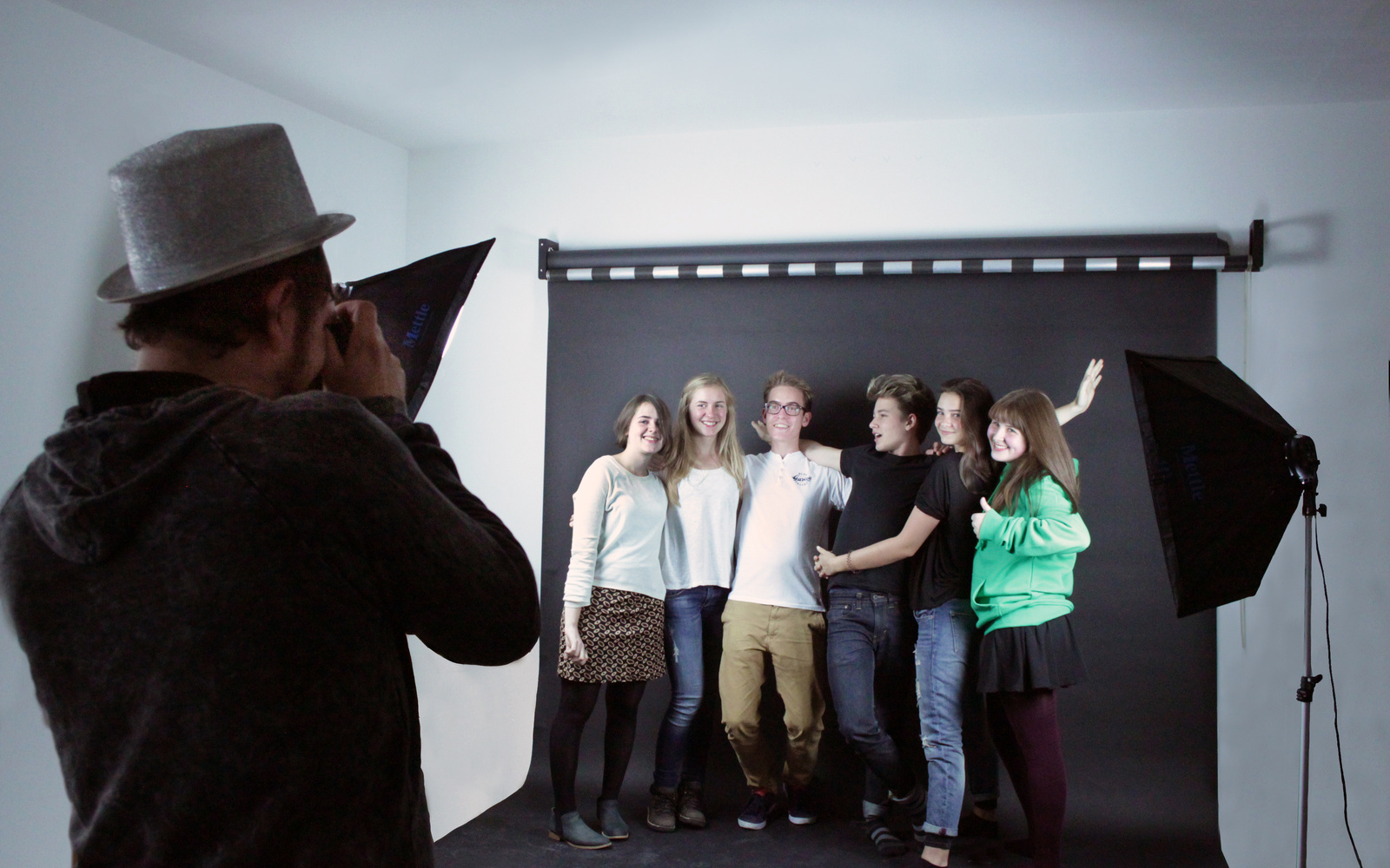 A group of young people in front of a black canvas laughing at the camera