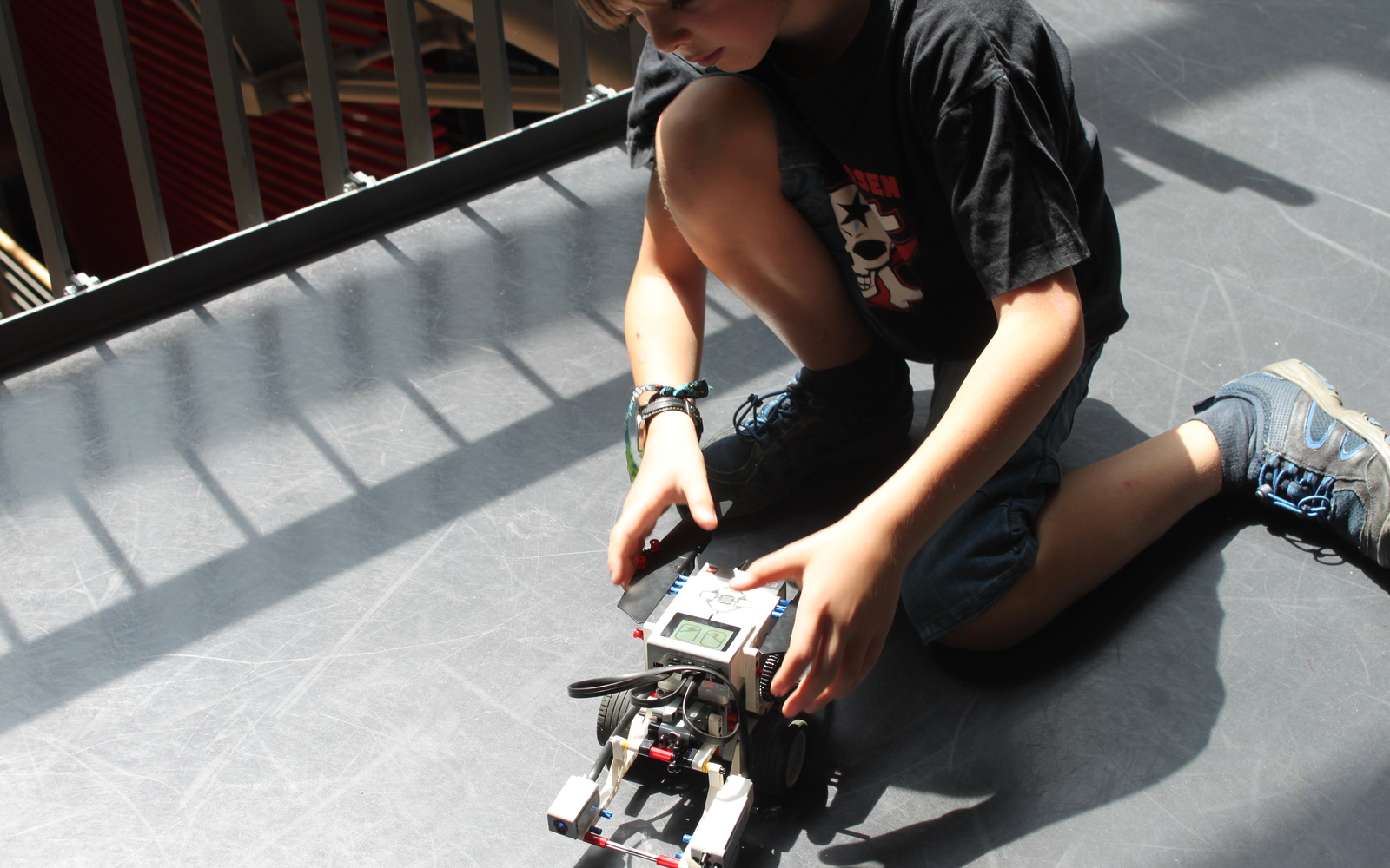 A boy is kneeling on the floor next to a lego-robot.