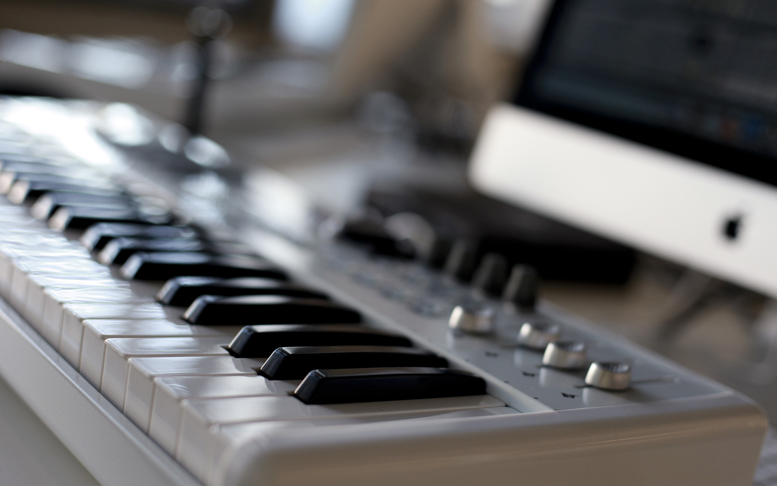 A keyboard in a close shot, that is attached to a computer in the background.