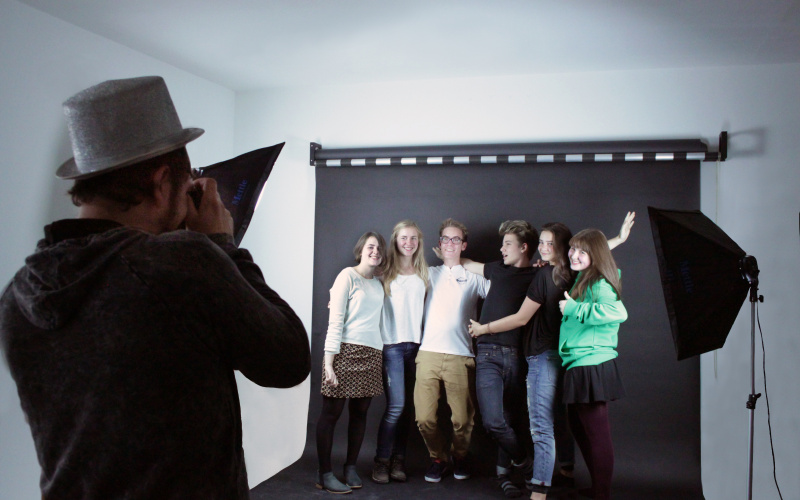 A group of young people in front of a black canvas laughing at the camera