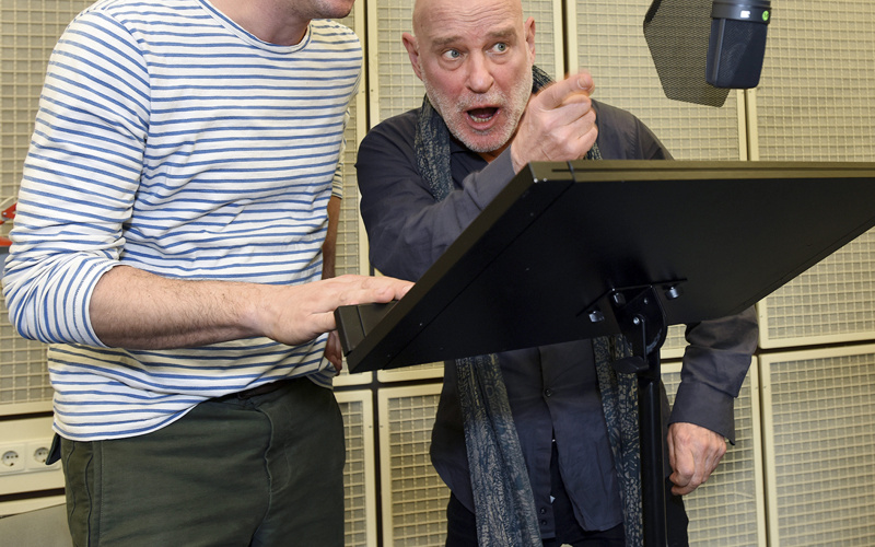 Two men in front of a desk and recording microphone