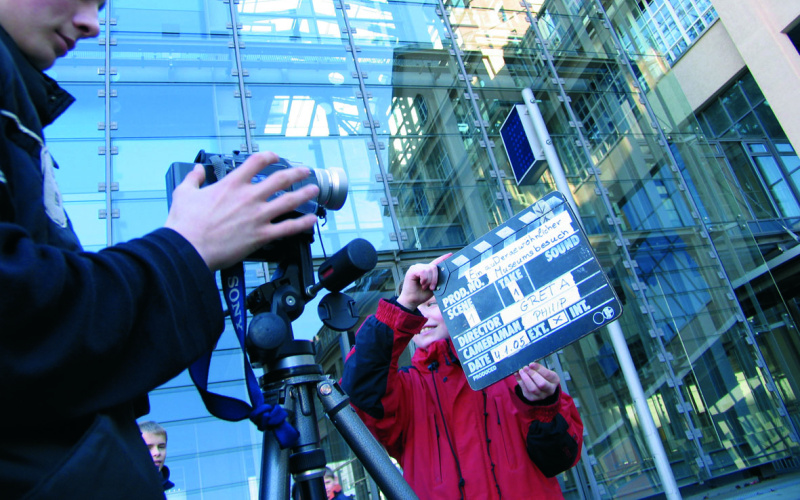 Someone is filming with a camera that is standing on a tripod. Somebody else is holding the clapper board in front of the camera.